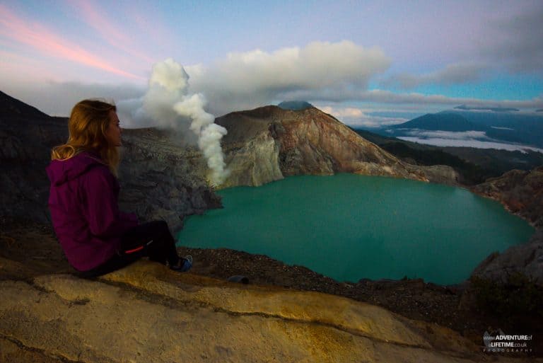 Dora sits on the crater of Ijen volcano looking down at the blue lake